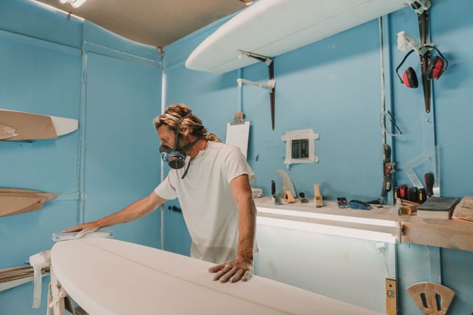 Man in respirator polishing surf board in workshop