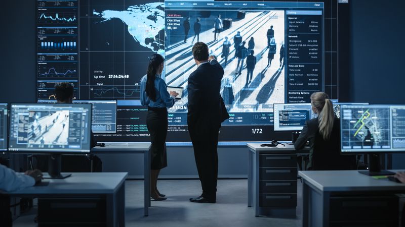 Professionals Analyze Surveillance Data on Large Screens in a Modern Control Room, Focusing on Security and Strategic Planning.