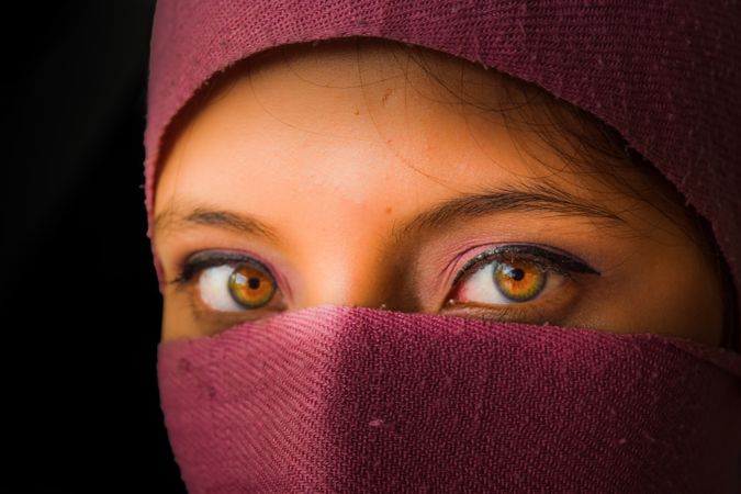 Woman showing her eyes behind purple fabric