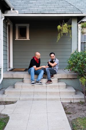 Man holding and kissing his dog sitting next to his friend outside on porch