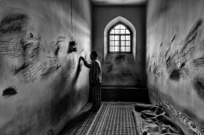 Grayscale photo of an older man standing in prison cell writing on the wall in Iraq