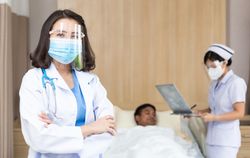Nurse taking care of patient on bed in hospital ward with doctor in foreground