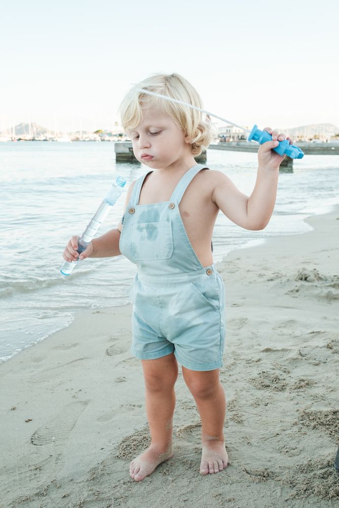Serious curious toddler playing with soap bubble toy on beach in