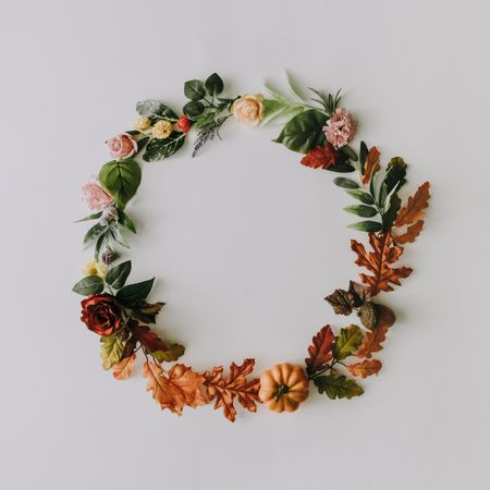 Wreath made of autumn fruits and leaves with summer flowers on light background