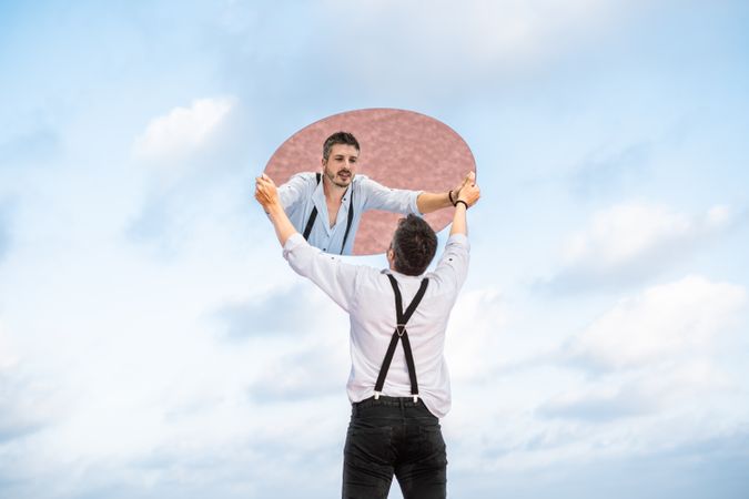Stylish man holding mirror up and reflecting