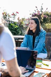 Young joyful woman working on the laptop chatting with her coworkers on a break on terrace outdoors.