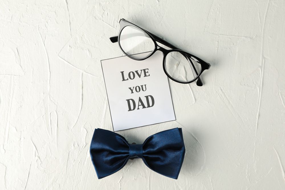 Inscription love you DAD, blue bow tie and glasses on blank background, space for text and top view