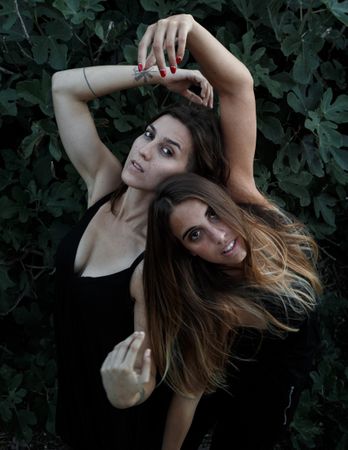 Young women posing near green bush