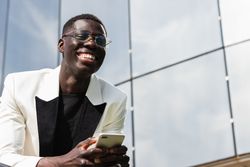 Content Black businessman with smartphone on city street