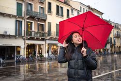 Asian female tourist with umbrella walking at city street on rainy weather