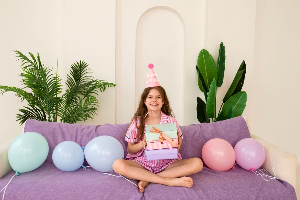 Young girl celebrating birthday at home with gifts and balloons.