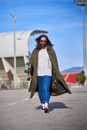 Stylish adult man in raincoat and jeans walking in park