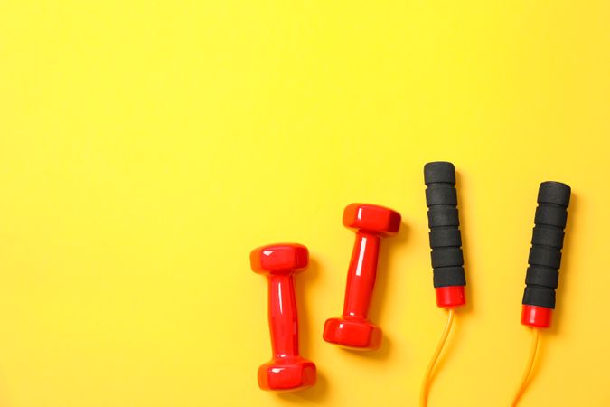 Dumbbells and jump rope on yellow background, space for text