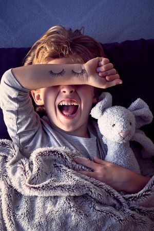Irritated boy covering eyes and creaming in bed