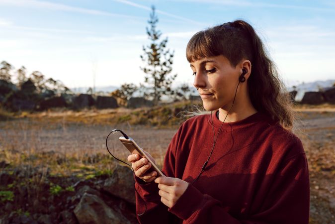 Young woman with piercing listening music on smartphone on hill