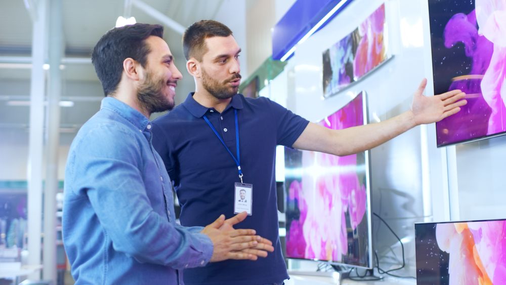 In the Electronics Store Professional Consultant Shows Latest 4K UHD TV's to a Young Man