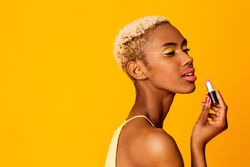 Black woman with short blonde hair applying lipstick