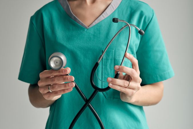 Crop surgeon showing stethoscope on light background