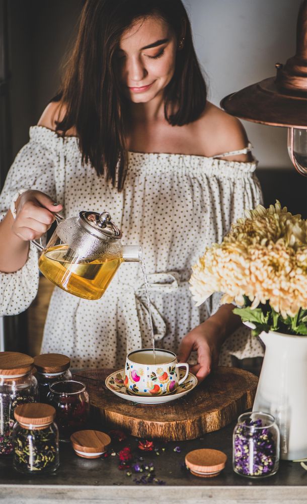 Woman pouring tea in floral cup and saucer from glass teapot