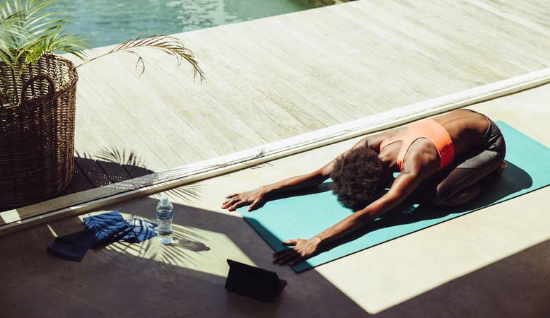 Black woman doing yoga outdoors by a swimming pool
