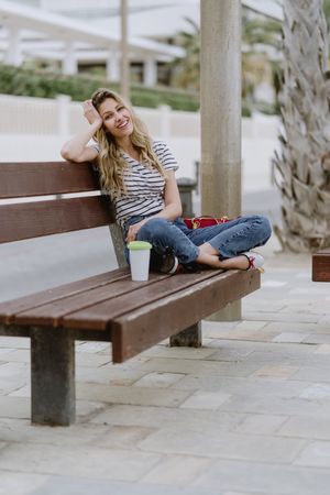 Happy woman with disposable cup of coffee sitting on street bench