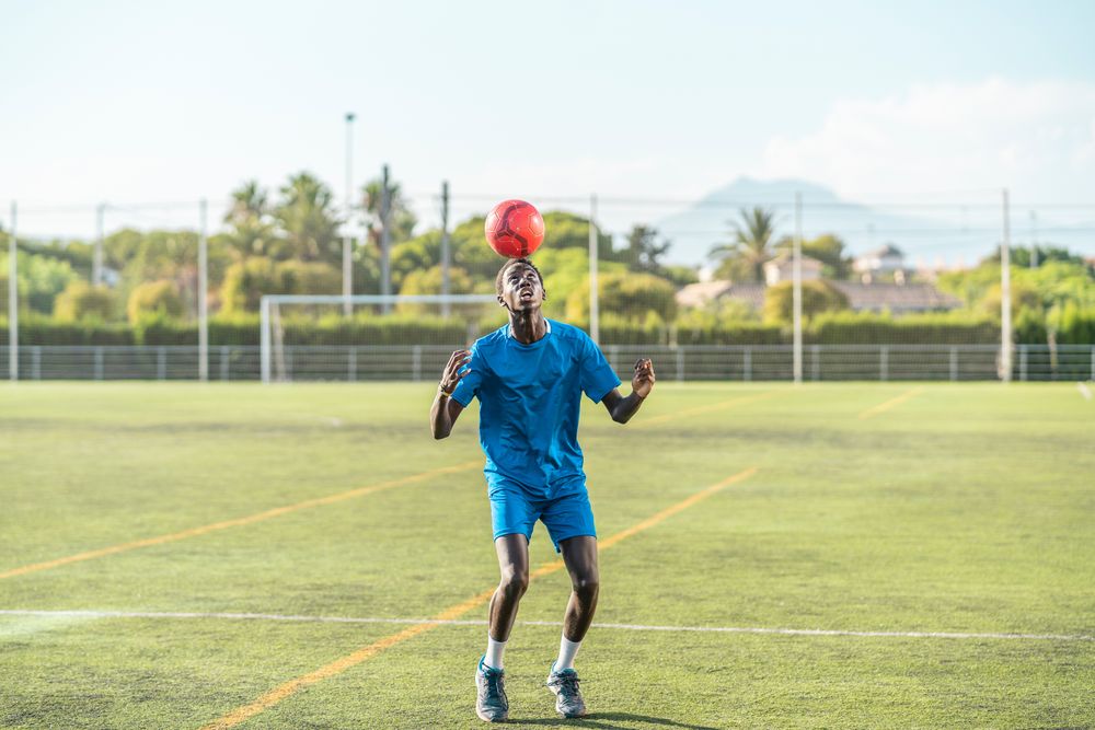 Black teenager jugging football ball on head