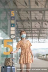 Woman with facemask beside her luggage at the airport 4ZMB95