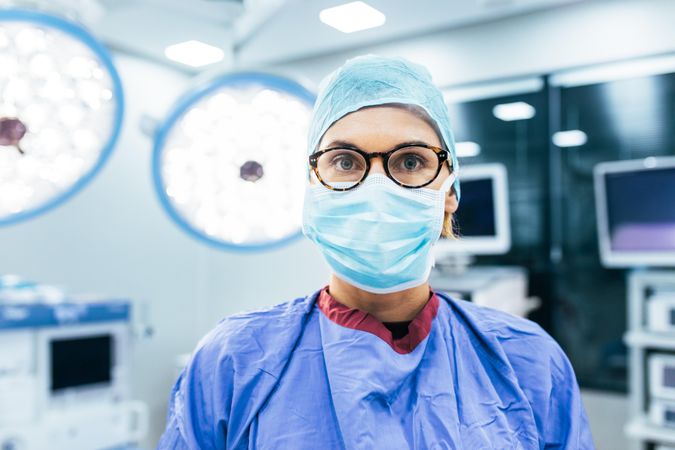 Close up portrait of female surgeon wearing surgical mask and scrubs in operation theater