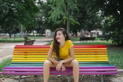 Cheerful woman sitting on rainbow bench