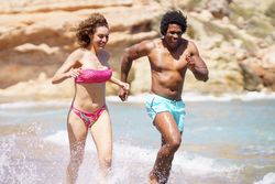 Black man and white woman running playfully along the coast