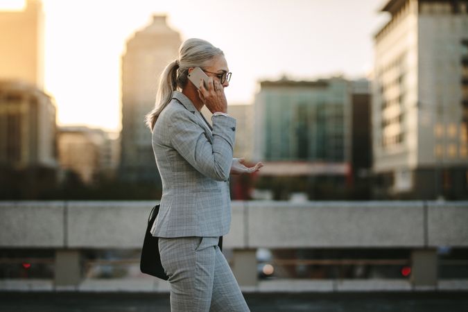 Older businesswoman using cellphone on city street with urban background