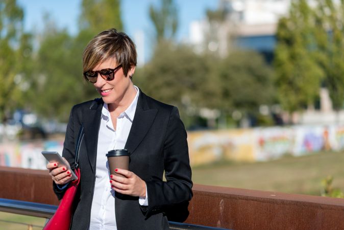 Businesswoman leaning on railing with coffee checking phone