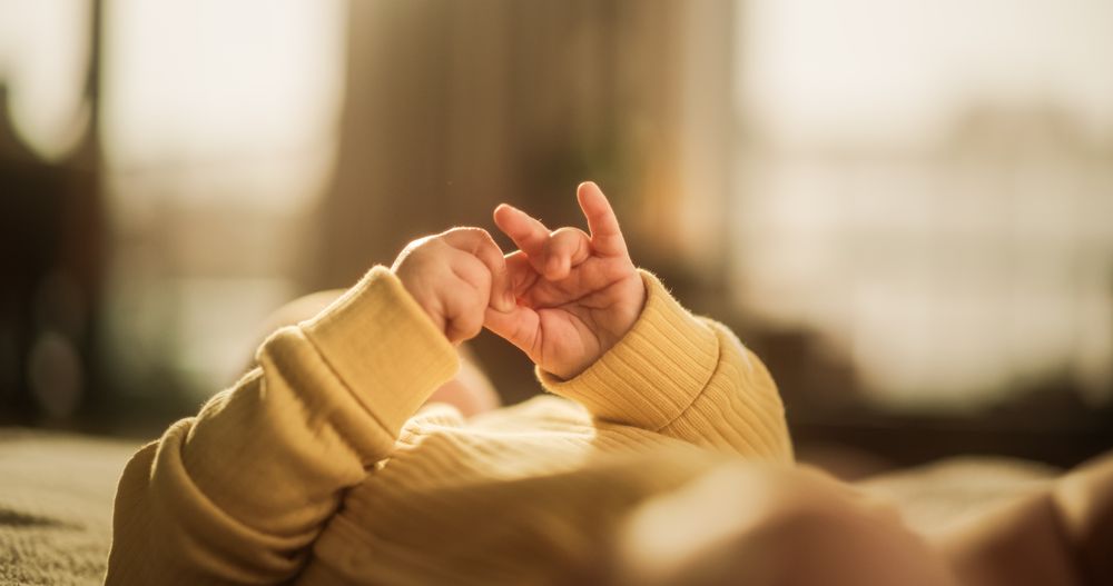 Close-Up on the Hands of a Cute Baby in a Yellow Jumper.