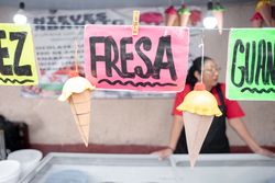 Nut and strawberry flavor signs in an ice cream street market stall with an Hispanic woman in the background