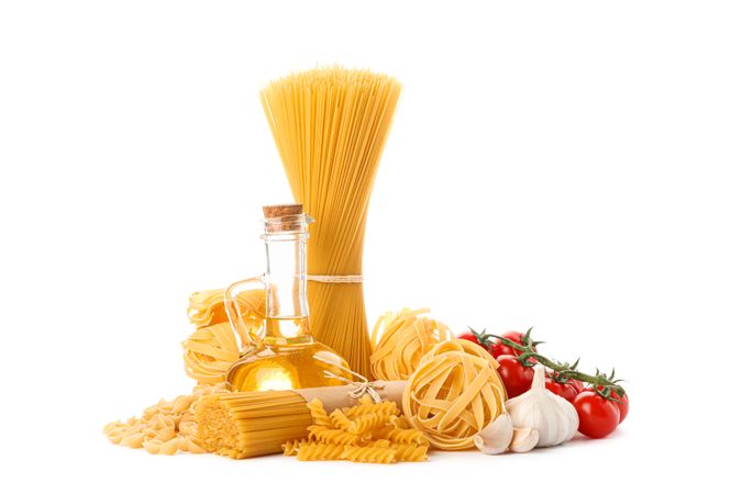 Pasta, olive oil, tomatoes and garlic isolated on bright background. Uncooked whole wheat pasta