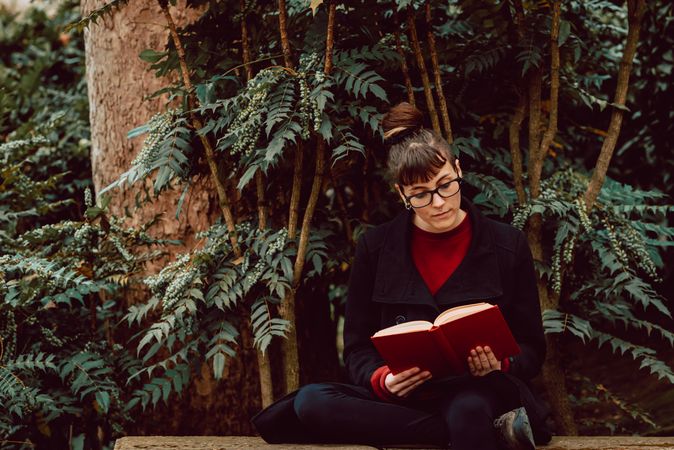 Young woman reading book on bench in park