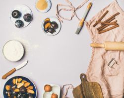 Baking ingredients and tools, plums, pastry brush, cinnamon, eggs on pastel background, copy space