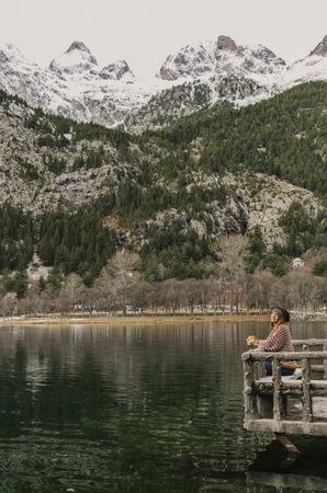Woman on seat near wonderful lake between hills in snow and cloudy sky