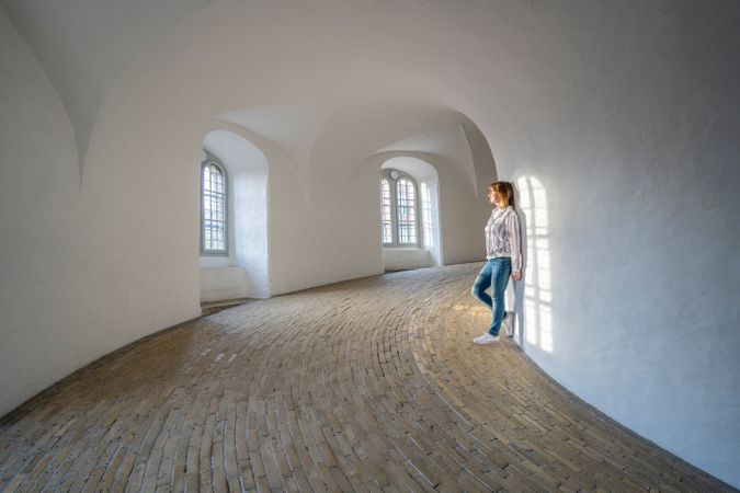 Casual woman leaning on wall in spacious gallery with windows