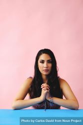 Hispanic woman praying with rosary beads in pink room, vertical 0vNmo0