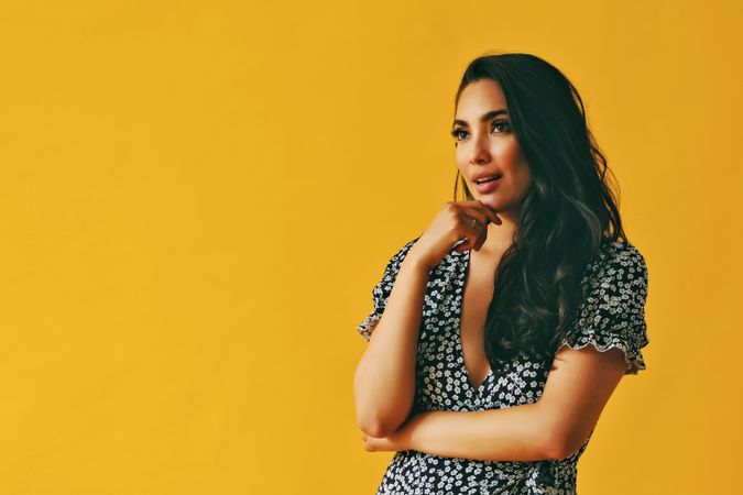 Amazed Hispanic woman wearing dress standing in yellow room