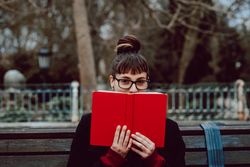 Young woman reading book on bench in park