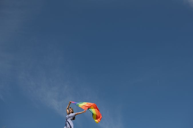 Young woman with rainbow banner against sky