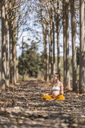 Calm adult pregnant woman practicing yoga while sitting in pose lotus on ground in park during sunny day