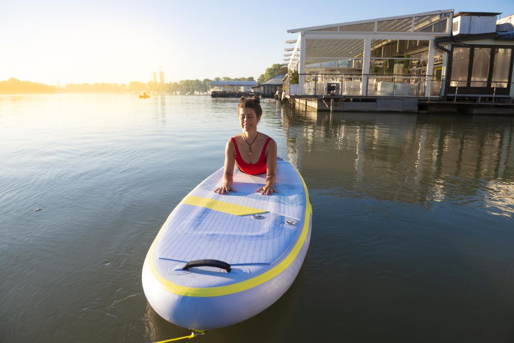 Woman stretching back on paddleboard in the water near pier