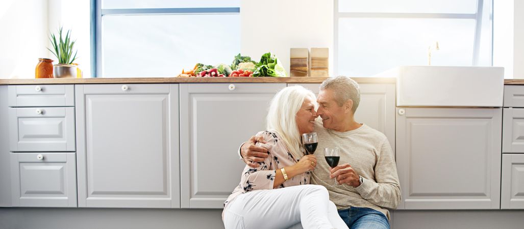 Wide shot of an older couple sitting on kitchen floor drinking red wine