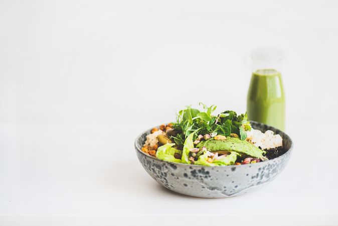 Healthy vegetarian bowl pictured on light background with smoothie on side, copy space