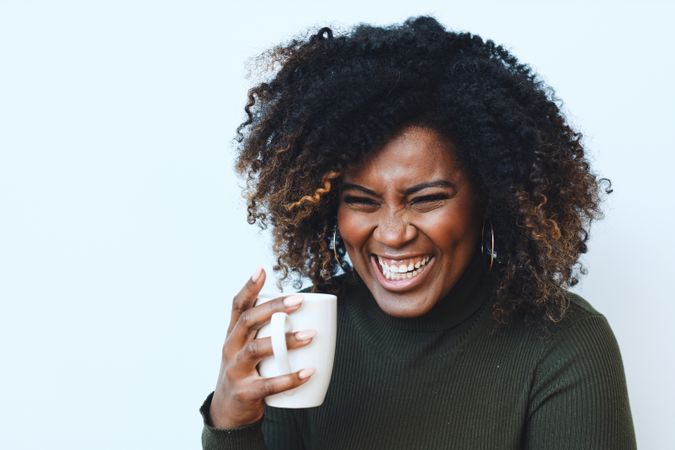 Happy Black woman laughing while holding a cup of coffee