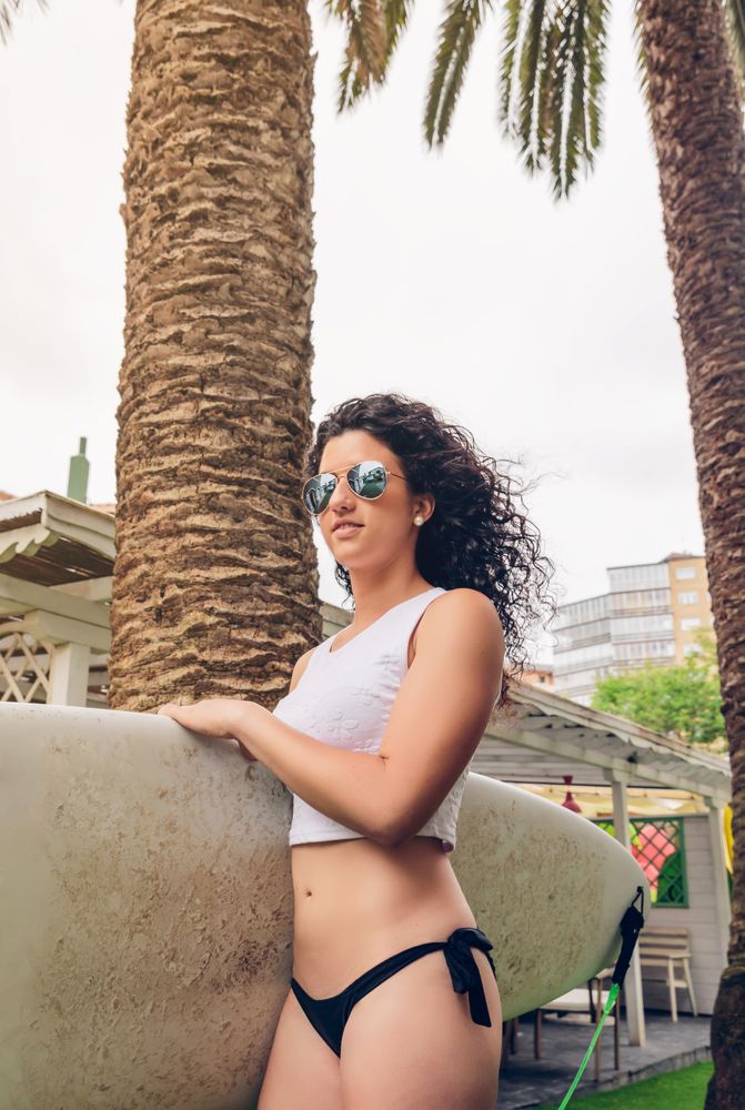 Brunette surfer woman with top and bikini holding surfboard by the clubhouse