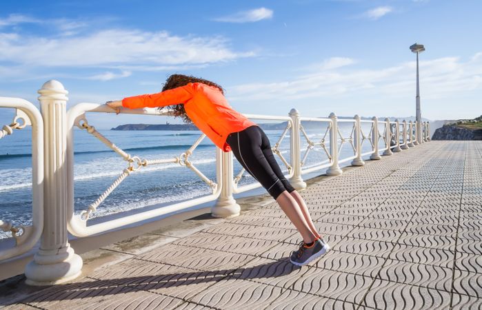 Fit woman stretching on railing before work out on the beach